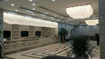 A hotel lobby with a marble reception desk, multiple flat-screen TVs, a large chandelier, and a patterned carpet.
