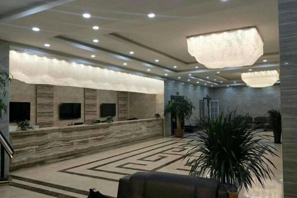 A hotel lobby with a marble reception desk, multiple flat-screen TVs, a large chandelier, and a patterned carpet.