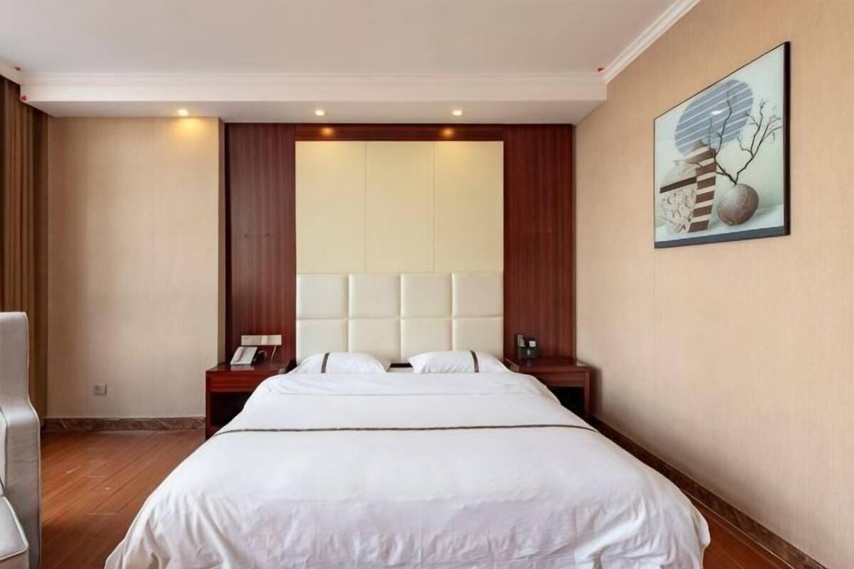 Een hotelkamer met een groot bed, een houten hoofdbord, een nachtkastje en een schilderij aan de muur.