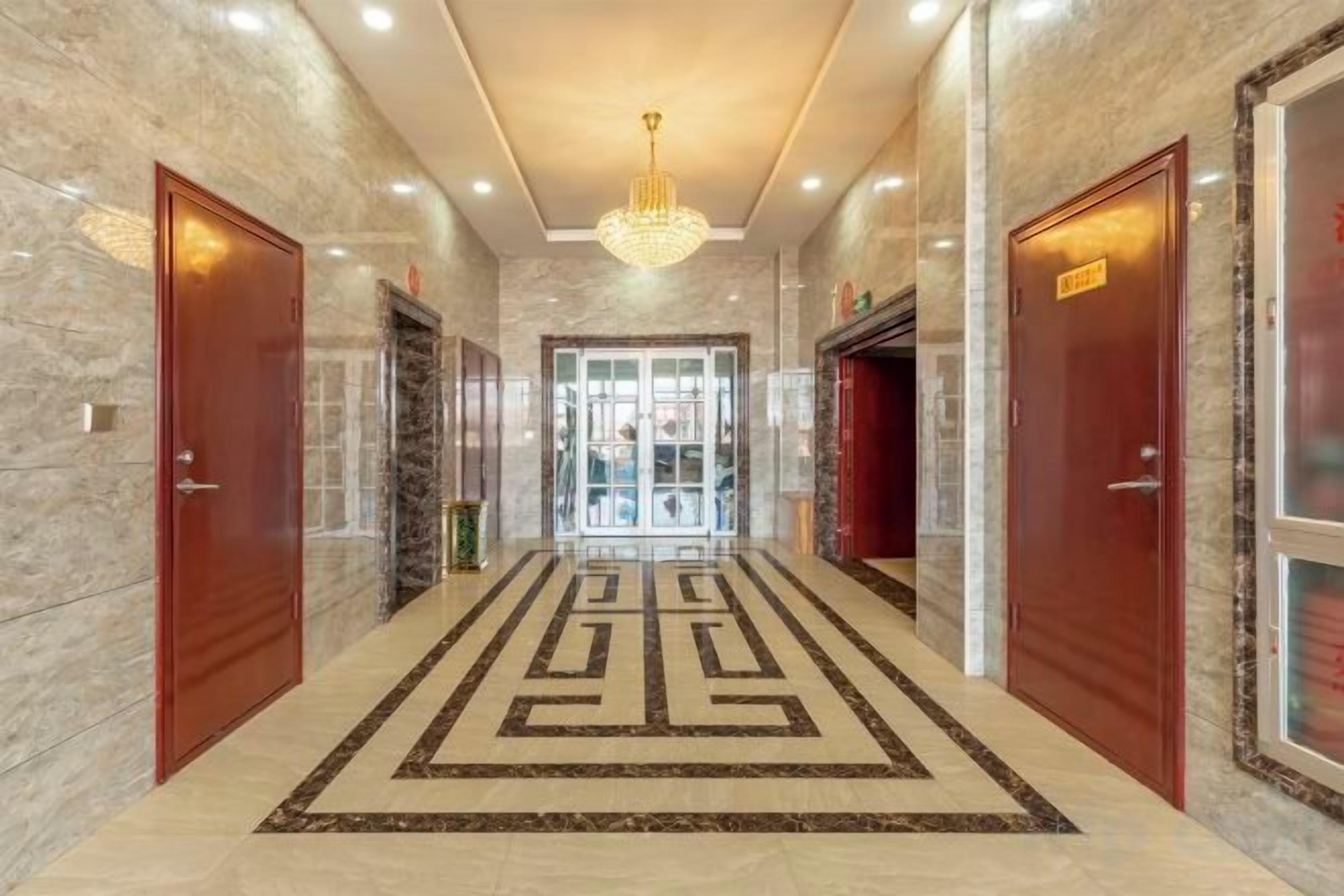 A hotel corridor with marble walls, a patterned carpet, and a chandelier.