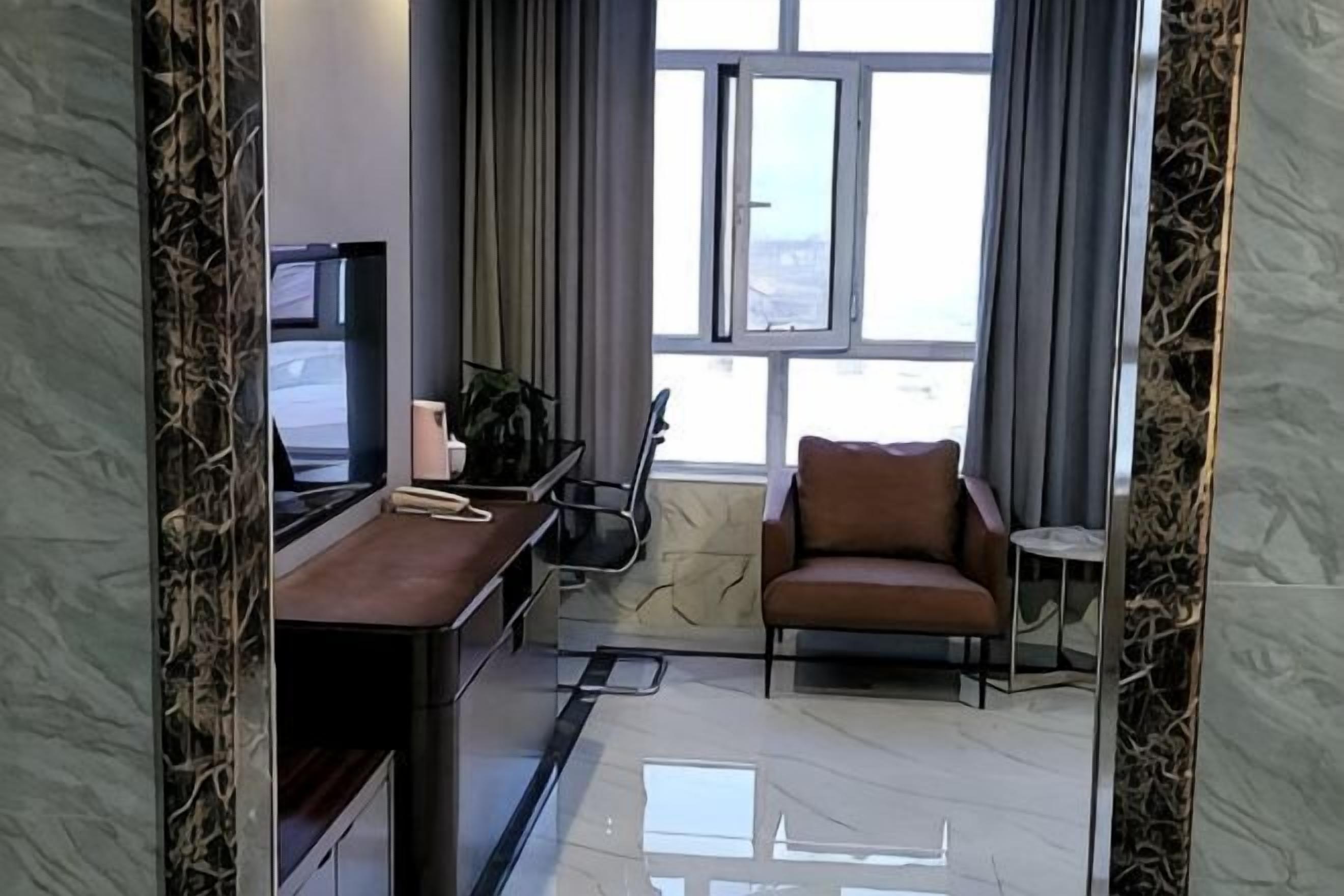 Une chambre d’hôtel moderne, dotée d’un bureau, d’une chaise et offrant une vue sur la ville grâce à de grandes fenêtres.
