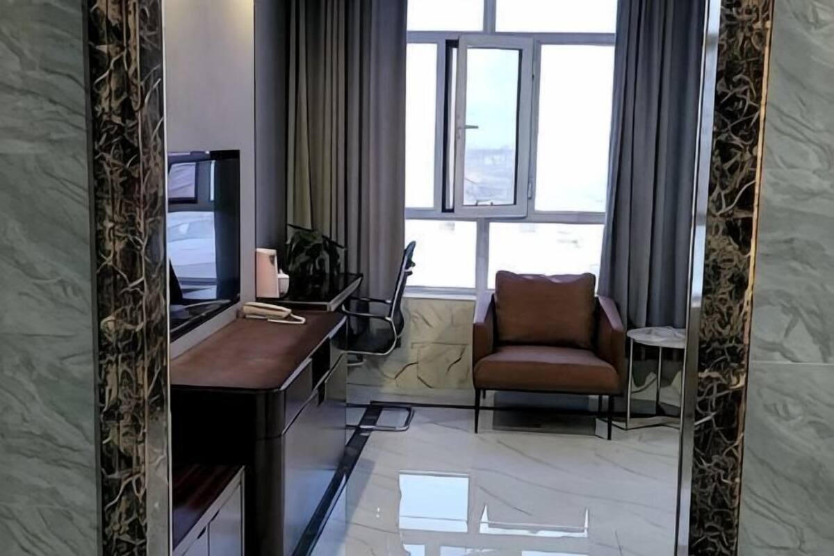 Een moderne hotelkamer met een bureau, stoel en uitzicht op de stad door grote ramen.