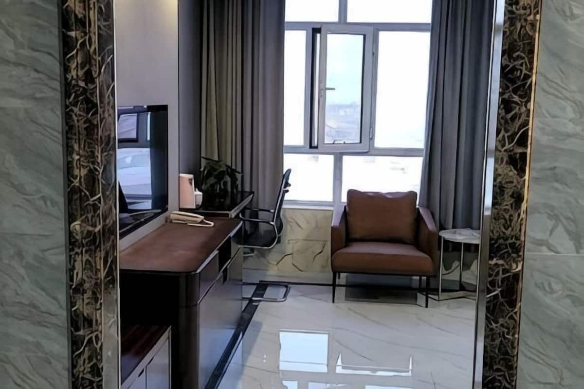 Une chambre d’hôtel moderne, dotée d’un bureau, d’une chaise et offrant une vue sur la ville grâce à de grandes fenêtres.