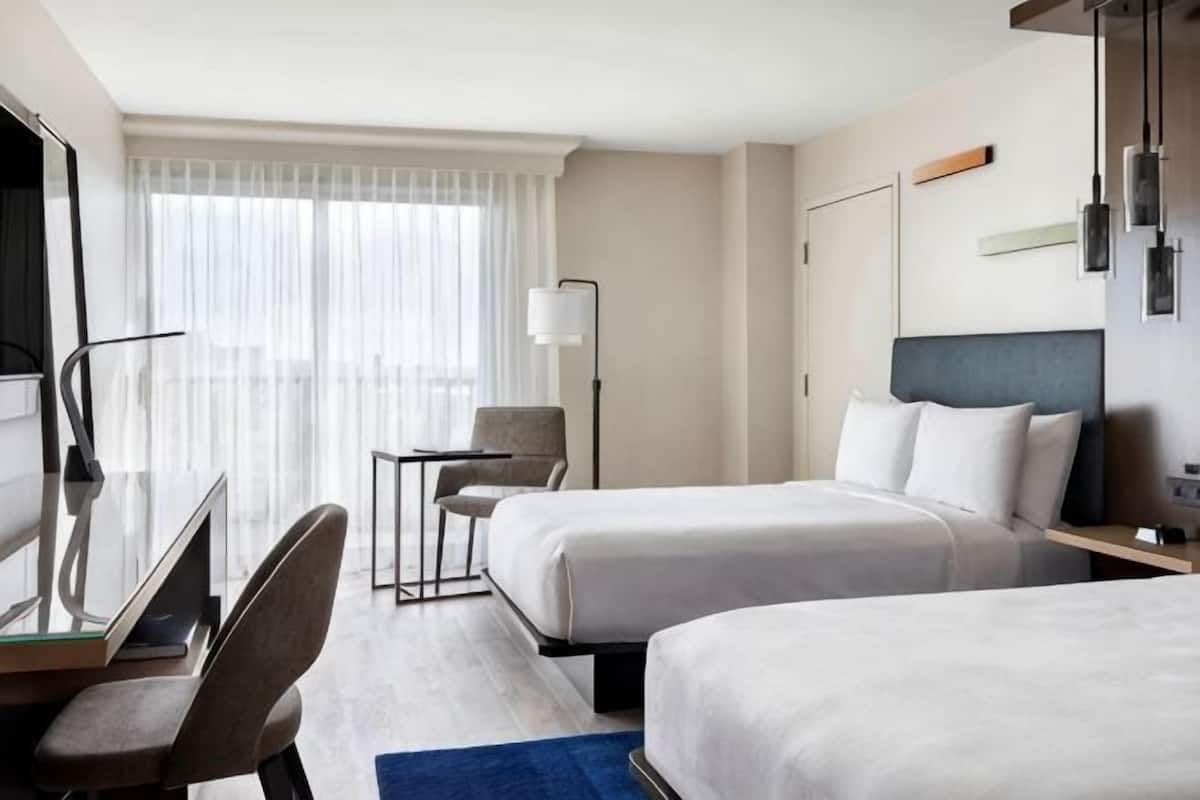 A hotel room with two beds, a desk, a chair, a TV, and a window with curtains.