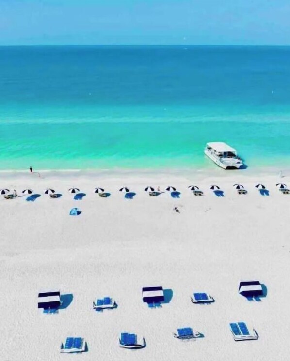 Une plage bordée de rangées de transats, avec un bateau sur l’eau.