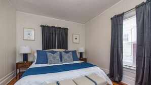 A neatly arranged bedroom with a large bed, two bedside tables with lamps, a bench at the foot of the bed, and a window with curtains.