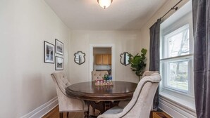 A dining room with a round table, four upholstered chairs, a potted plant, and framed pictures on the wall.