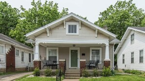A two-story house with a front porch, a green door, and a small front yard.