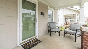 A porch with two chairs, a welcome mat, and a door with a glass panel.