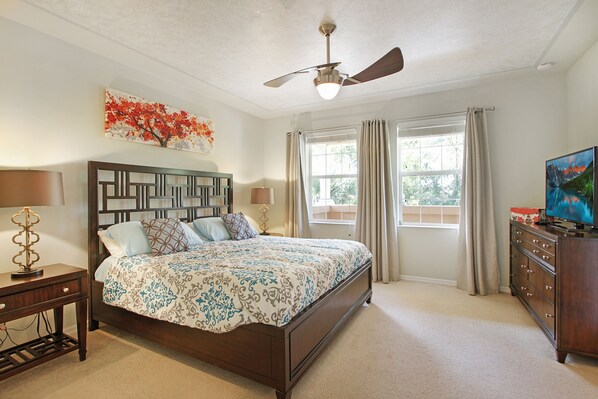 A bedroom with a bed, a nightstand, a dresser, a ceiling fan, and a window with curtains.