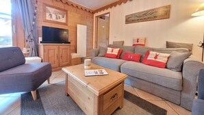 Un salon chaleureux avec un canapé gris, une table basse en bois, un téléviseur et un tableau accroché au mur.
