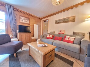 A cozy living room with a grey sofa, a wooden coffee table, a television, and a painting on the wall. - At the feet of ski slopes main flat 3 bedrooms for 6/8 persons (Chantemerle)