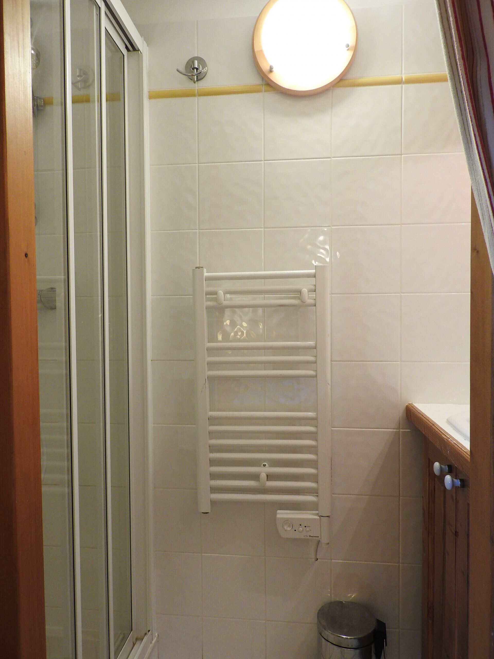 A bathroom with white tiles, a glass shower enclosure, a towel rack, and a toilet.