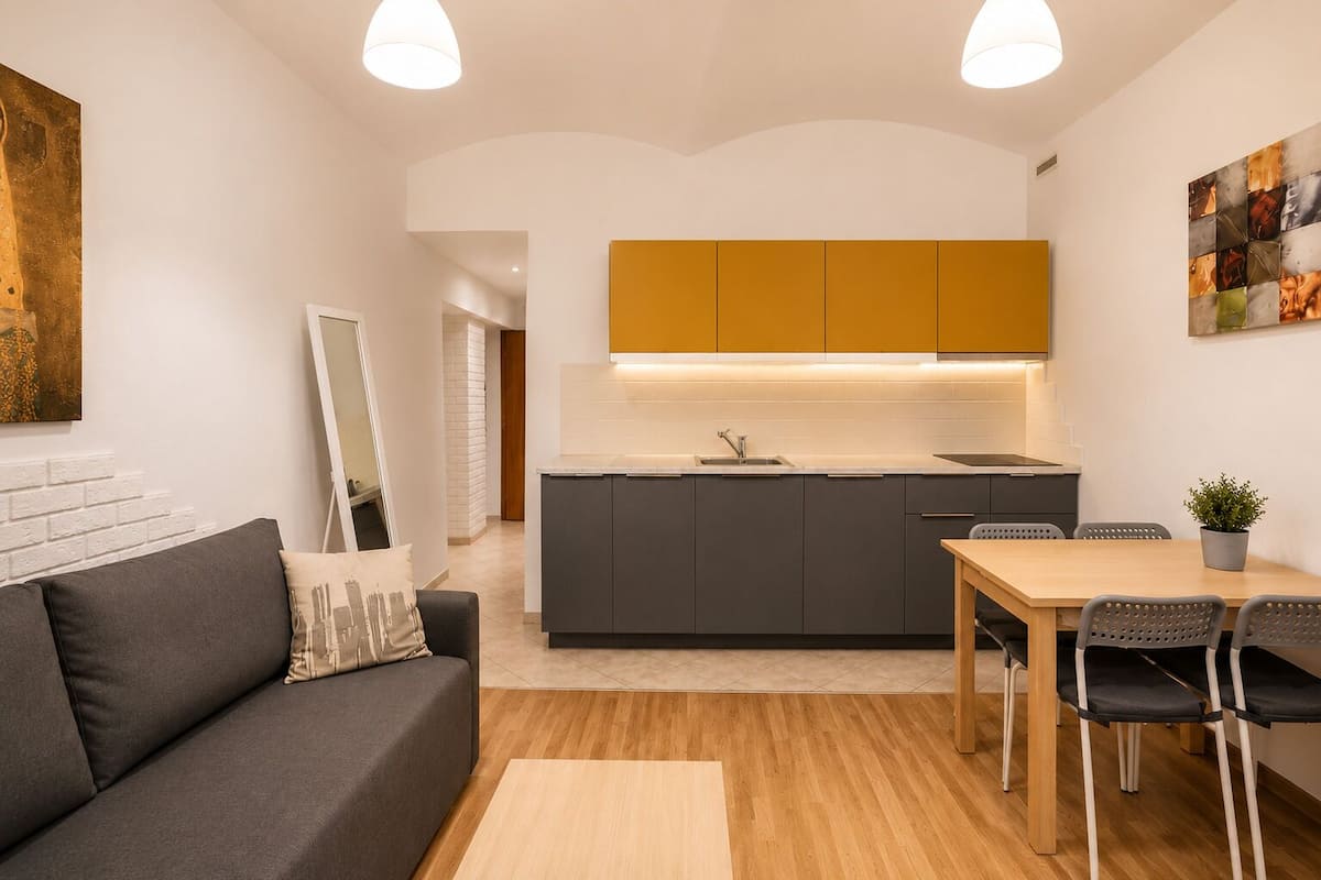 A modern kitchen with grey cabinets, a wooden dining table, and a grey sofa.