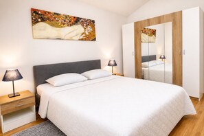 A bedroom with a bed, bedside lamps, a nightstand, a wardrobe, and a painting on the wall.