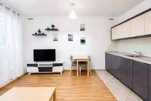 Moderni keittiö, jossa on sisäänrakennettu astianpesukone, ruokailutila puupöydällä ja -tuoleilla sekä litteänäyttöinen televisio valkoisessa kaapissa.