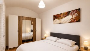 A bedroom with a bed, bedside lamps, a wooden wardrobe, and a painting on the wall. - Ground Floor Apartment (Prague)