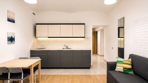 A compact living space with a kitchenette, a dining area, and a seating area with a sofa and a small table. - Ground Floor Apartment (Prague)