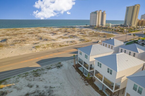 A coastal residential area with beachfront properties, a road, and high-rise buildings in the background.