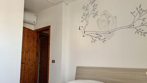 A bedroom with a bed, a wooden door, and a wall mural of birds on a branch. - M324 - Marcelli, delightful three-room apartment with panoramic terrace (Marcelli)