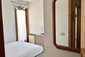 Un dormitorio con cama, cómoda, radiador, lámpara y espejo.