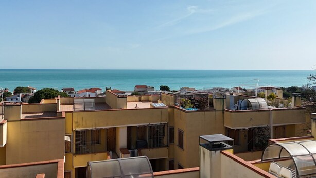 A residential area with multiple buildings, some with flat roofs and others with sloped roofs, overlooking a body of water. - M324 - Marcelli, delightful three-room apartment with panoramic terrace (Marcelli)