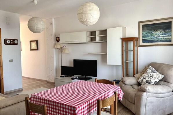 Una habitación con una mesa a cuadros, un sofá, un televisor y un cuadro en la pared.