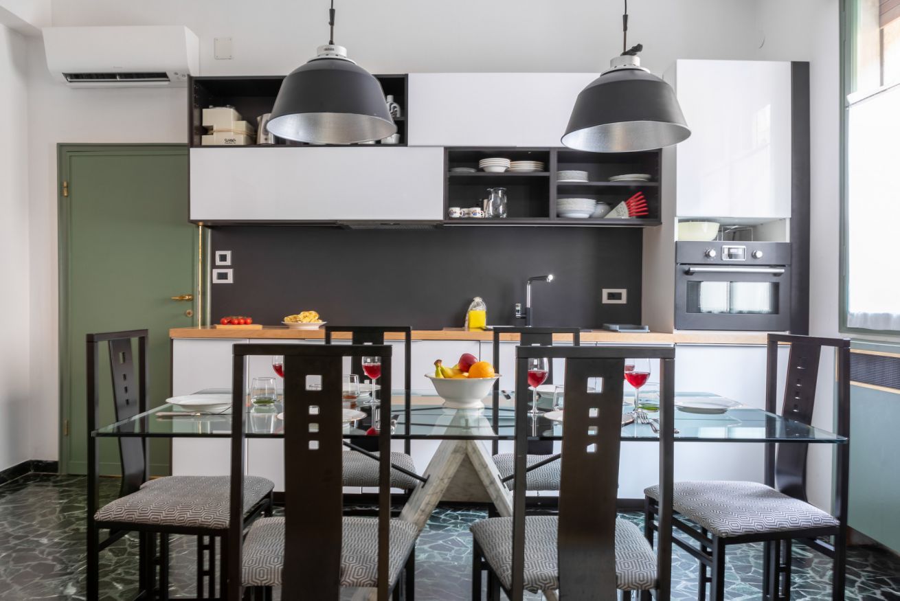 Une cuisine moderne avec une table à manger en verre, des chaises noires et des luminaires suspendus.