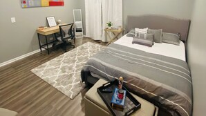 Une chambre à coucher avec un lit, un bureau, une chaise, une petite table et une fenêtre avec des rideaux.