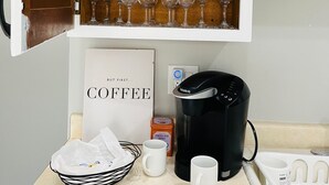 Une cuisine équipée d’un coin café, comprenant une machine à café Keurig, des tasses et un panneau indiquant : « MAIS D’ABORD… UN CAFÉ ».