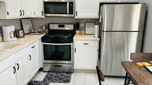 Une cuisine moderne avec des armoires blanches, un réfrigérateur en acier inoxydable, un four à micro-ondes, une cuisinière et une machine à café.