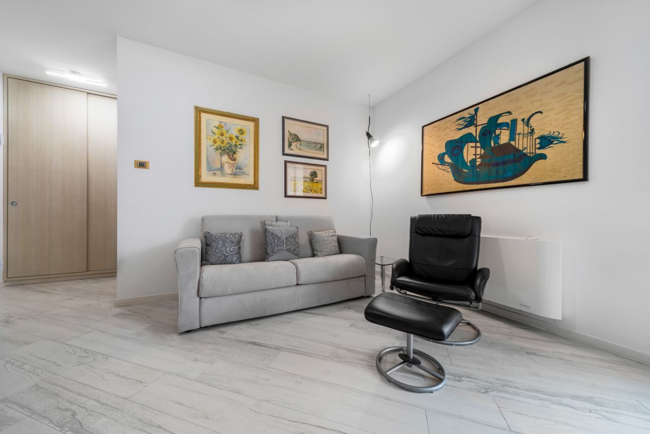 Ein Zimmer mit einer grauen Couch, einem schwarzen Sessel und einer Holztür.