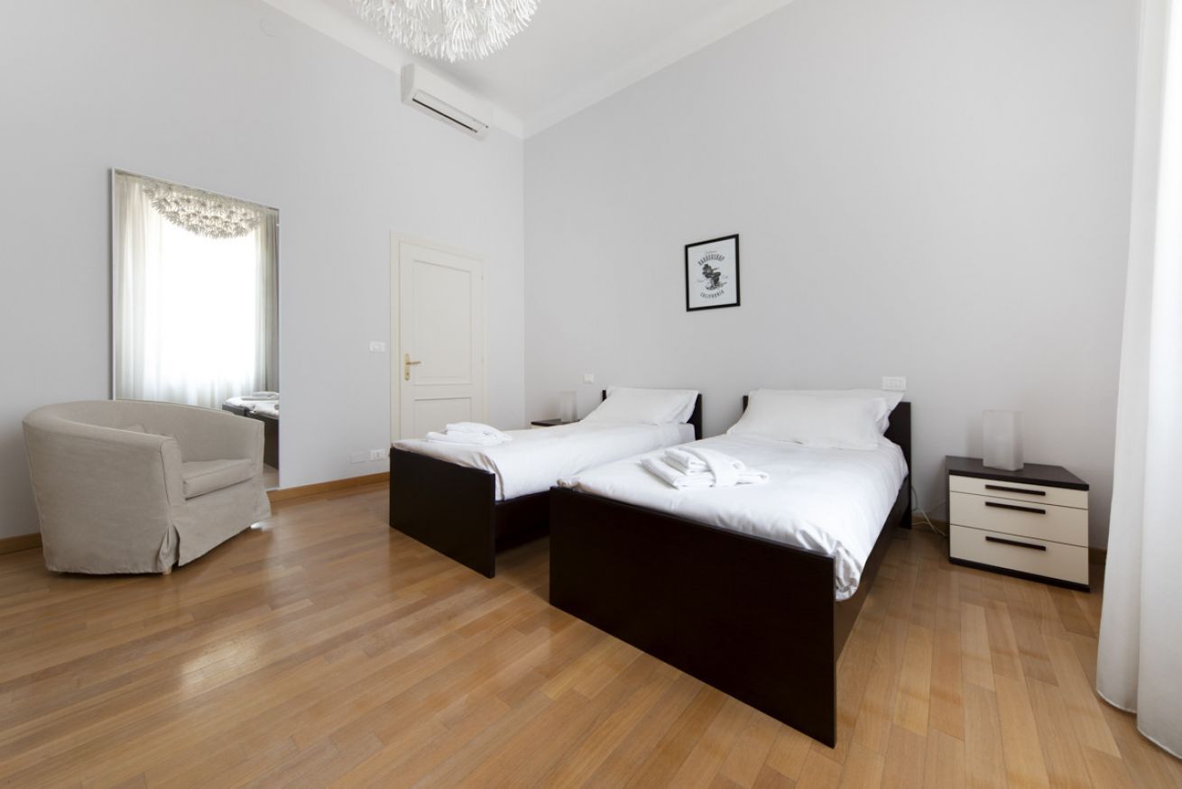 A modern bedroom with two beds, a chair, a bedside table, and a framed picture on the wall.