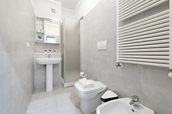 A modern bathroom with a toilet, bidet, sink, and a glass shower enclosure.