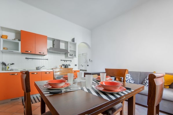 A modern kitchen with orange cabinets, a dining table set with orange plates, and a gray sofa in the living area.