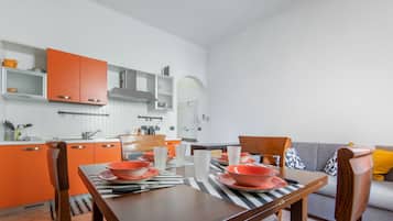 Eine moderne Küche mit orangefarbenen Schränken, einem Essplatz mit orangefarbenen Tellern und einem grauen Sofa im Wohnbereich.