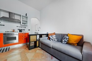 Ett modernt kök med en grå soffa och orange skåp.
