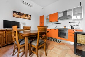 Ett modernt kök med orange skåp, ett matbord i trä och en svart spis.