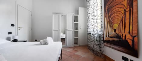 A hotel room with a bed, a wardrobe, a bathroom, and a corridor with a patterned curtain.