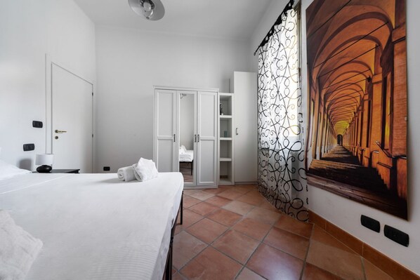 A hotel room with a bed, a wardrobe, a bathroom, and a corridor with a patterned curtain.