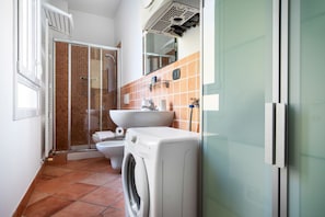 A compact bathroom with a glass shower enclosure, a white washing machine, a sink, and a toilet.