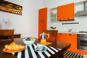 Ett kök med orange skåp, en spis och en kaffebryggare på ett träbord med en randig bordsduk.