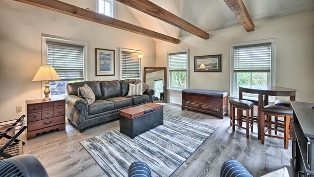 A spacious living room with a large sofa, a coffee table, and a dining area with a table and chairs. There are windows with blinds, a lamp, and a fireplace. - A cozy, beautifully renovated 1829 farmhouse (Mechanicsburg)