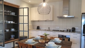 A modern kitchen with white cabinets, a wooden dining table set with white bowls and plates, and a hanging pendant light. - Cozy apartment, full equipped, in a gated community, close to places of interest (Sint Michiel)