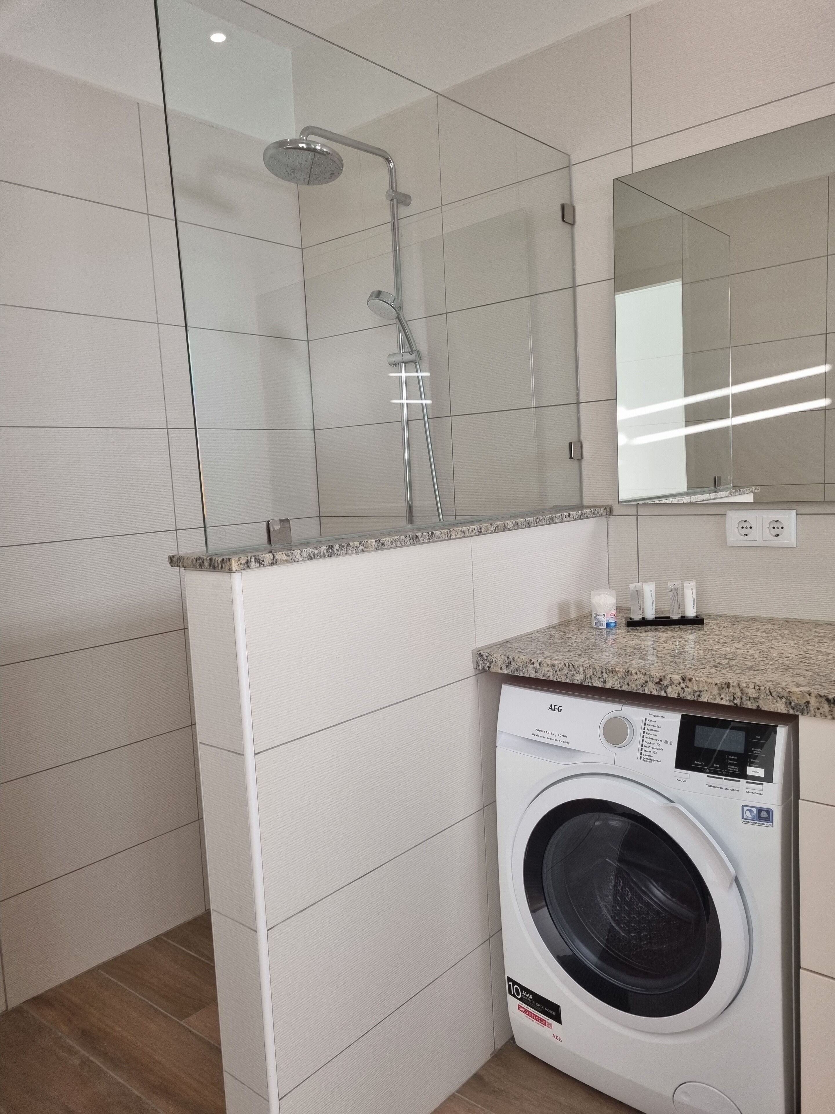 A modern bathroom with a built-in washing machine, a shower, and a large mirror.