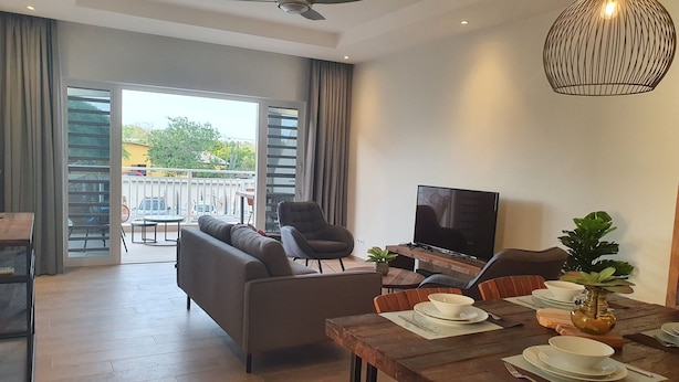 A modern living room with a sofa, TV, dining table, and a balcony with a view. - Cozy apartment, full equipped, in a gated community, close to places of interest (Sint Michiel)