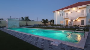 A swimming pool with a tiled deck, a two-story building with a balcony, and a staircase leading to the upper floor. - Cozy apartment, full equipped, in a gated community, close to places of interest (Sint Michiel)