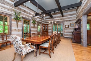 A log cabin interior with a large dining table, wooden chairs, and a chandelier.