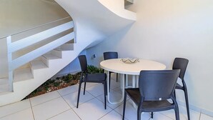 Un intérieur moderne avec un escalier blanc, une table ronde entourée de quatre chaises et un petit espace jardin.