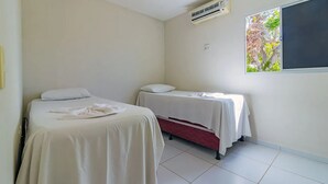 Une petite chambre propre, avec deux lits, une fenêtre donnant sur des arbres et un appareil de climatisation.